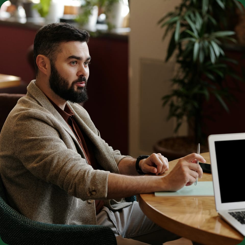 A man at a cafe table with a laptop, mid-conversation